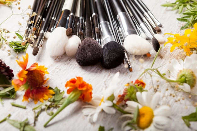 Pinceles de maquillaje cosmético junto a flores silvestres sobre fondo de madera