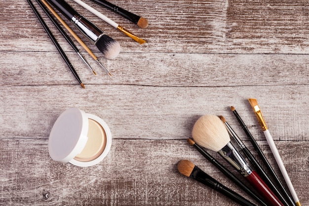 Pinceles de maquillaje y otros productos cosméticos sobre fondo de madera. En la imagen de la vista superior