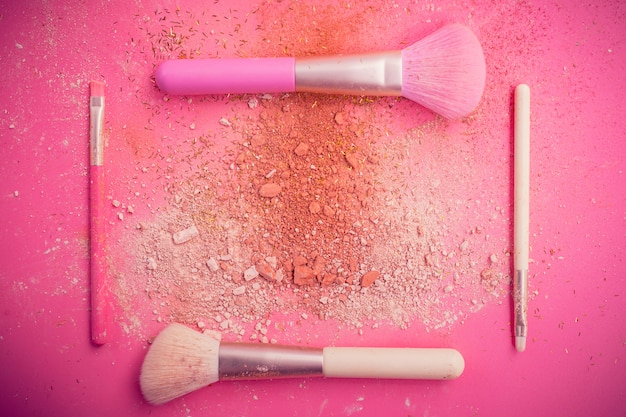 Pinceles de maquillaje con polvo sobre fondo rosa