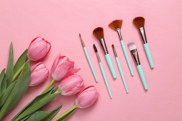Pinceles de maquillaje y tulipanes rosas sobre fondo rosa Concepto de belleza romántica