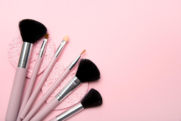 Los pinceles de maquillaje yacen sobre esponjas cosméticas sobre un fondo rosa con espacio para copiar