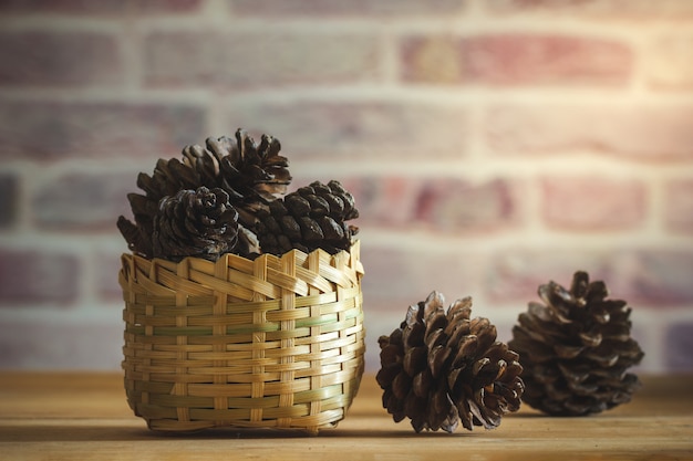 Pine Cone im Bambuskorb auf Holztisch- und Backsteinmauerhintergrund mit Morgensonnenlicht.