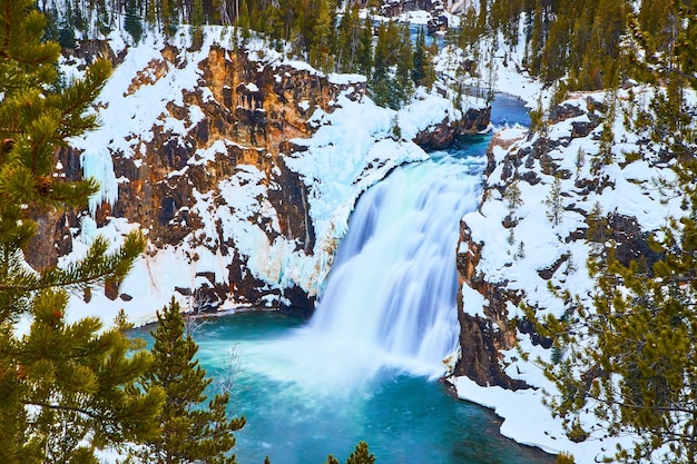 Pinheiros emolduram penhascos nevados e impressionantes cachoeiras azuis em Yellowstone