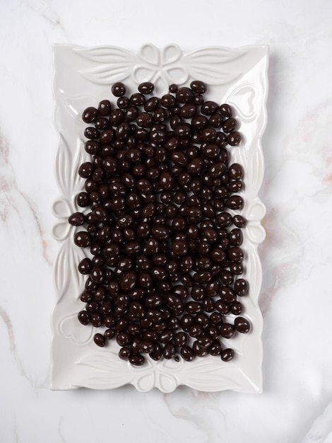 Pinienkerne in Schokoladenglasur oder Dragee auf einer weißen quadratischen Platte von oben