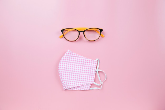 Pinkes Plaid der chirurgischen Maske und orangefarbene Brille auf dem flachen Backlay-Flatlay-Draufsicht-Copyspace im Hintergrund