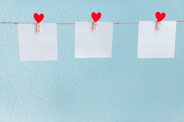 Pinos dos corações do amor do Valentim vermelho que penduram no cabo natural contra o fundo azul. Mock-se conceito para o seu texto