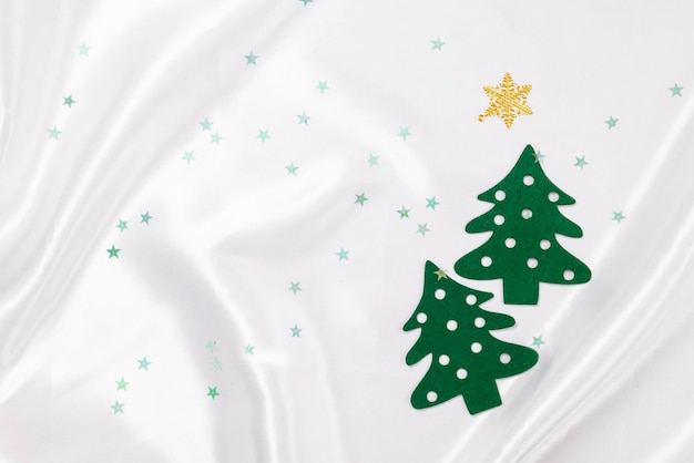 Pinos verdes hechos de tela de fieltro con adornos de Navidad de oro sobre fondo de seda blanca.