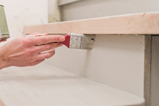 Pinsel in der Hand, während der Reparatur Farbe auf eine Holzoberfläche auftragen