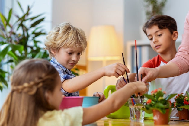 Pinsel in Wasser. Die Schüler stecken ihre Malpinsel in ein Glas mit Wasser, bevor sie mit dem Lehrer malen