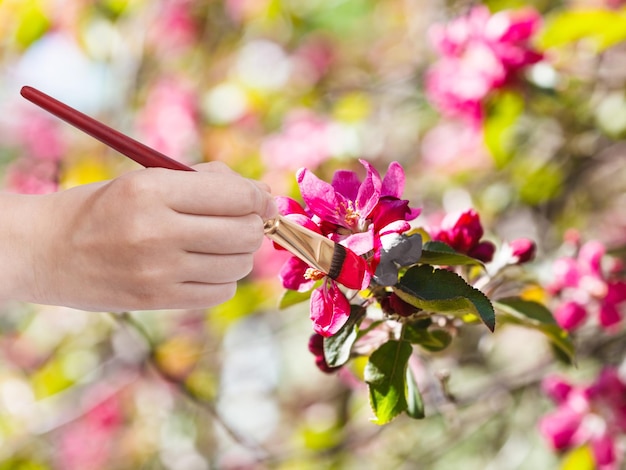 Pinsel malt rote Blumen auf Apfelbaum