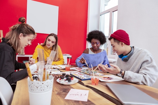 Pinsel und Zeichnung. Vier talentierte stilvolle Kunststudenten halten ihre Malpinsel beim Zeichnen