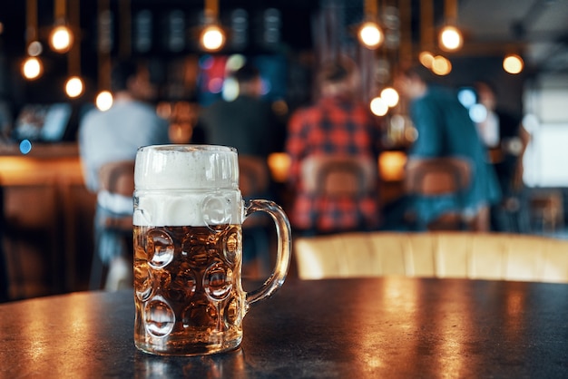 Pint Glas kaltes frisches Bier mit Schaum auf dem Tisch in der Kneipe mit Leuten