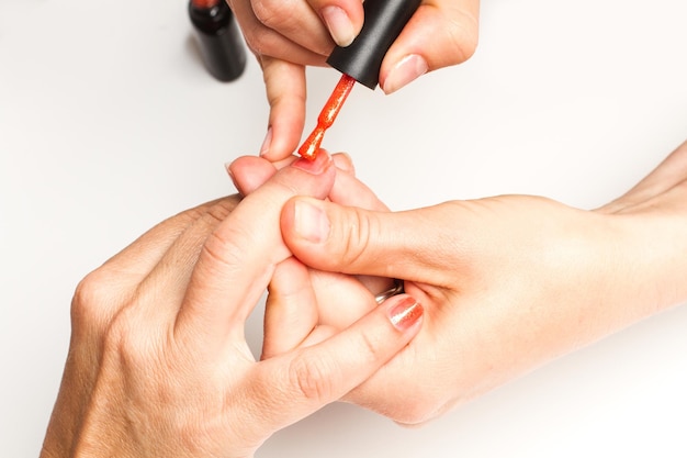 Pintando as unhas com esmalte vermelho na mão da mulher