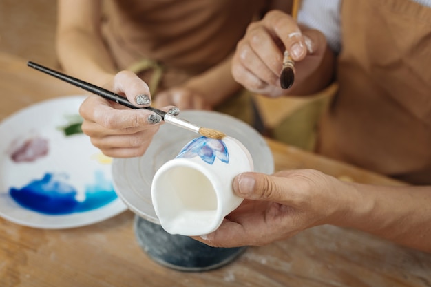 Pintar flores. Pareja de artistas profesionales creativos pintando algunas flores en una pequeña olla de barro