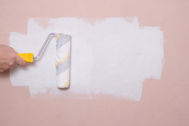 Pintar las paredes con un rodillo de pintura de color rosa con pintura blanca reparaciones en el hogar