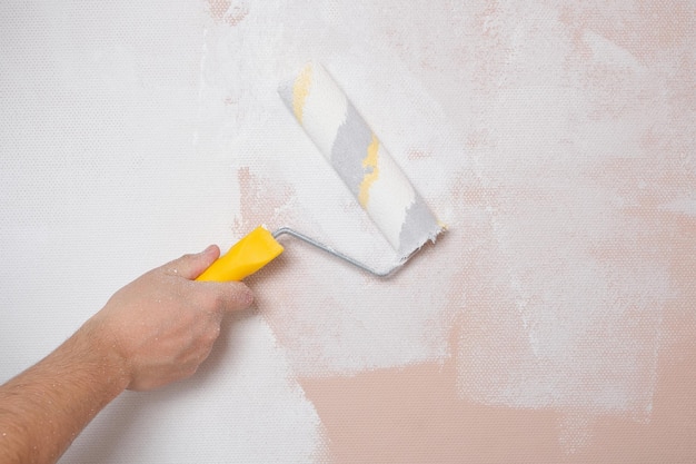 Pintar las paredes con un rodillo de pintura de color rosa con pintura blanca reparaciones en el hogar