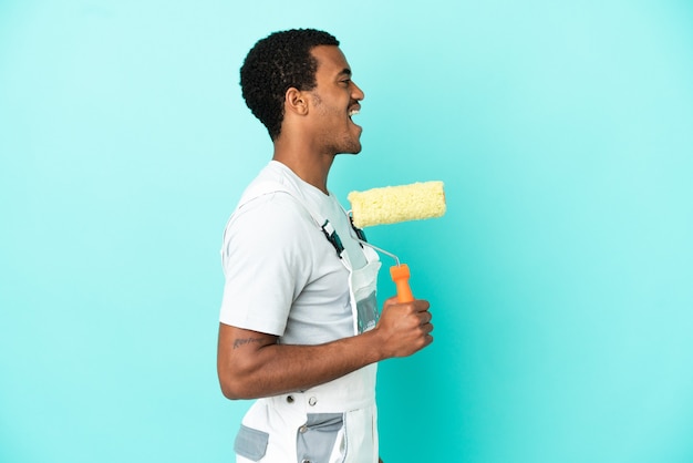 Pintor afroamericano hombre sobre fondo azul aislado riendo en posición lateral