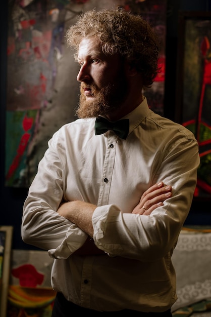 Pintor barbudo con traje sentado en la galería cerca de sus pinturas