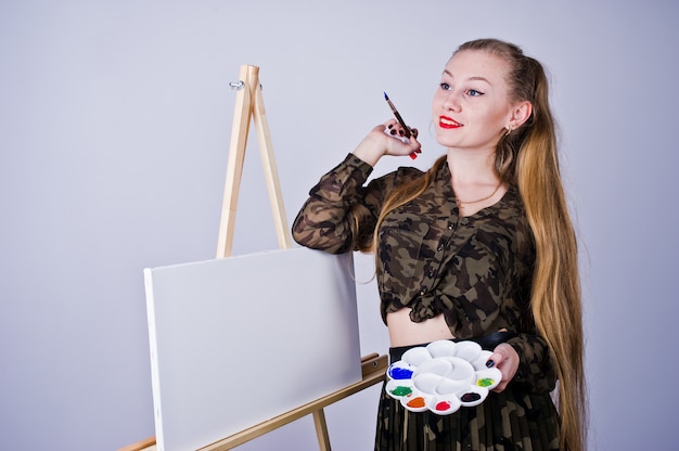 Pintor bonito do artista da mulher com escovas e levantamento da lona do óleo isolado no branco.