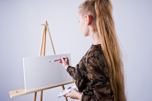 Pintor bonito do artista da mulher com escovas e levantamento da lona do óleo isolado no branco.