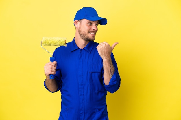 Pintor brasileiro isolado em fundo amarelo apontando para a lateral para apresentar um produto