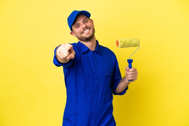 Foto pintor brasileiro isolado em fundo amarelo apontando para frente com expressão feliz