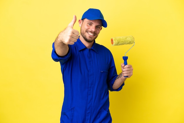 Pintor brasileiro isolado em fundo amarelo com polegar para cima porque algo bom aconteceu