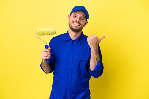 Pintor brasileño aislado sobre fondo amarillo apuntando hacia el lado para presentar un producto