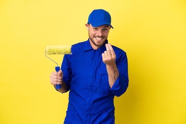 Pintor brasileño aislado sobre fondo amarillo haciendo gesto de dinero