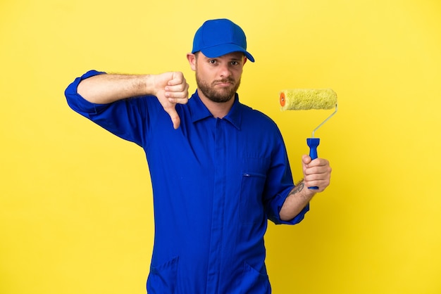 Pintor brasileño aislado sobre fondo amarillo mostrando el pulgar hacia abajo con expresión negativa