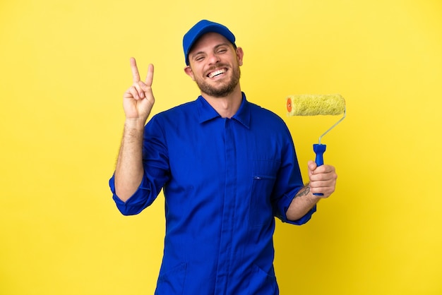 Pintor brasileño aislado sobre fondo amarillo sonriendo y mostrando el signo de la victoria