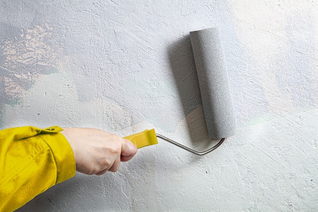 Pintor de casa en traje amarillo pinta la pared en color gris con rodillo de pintura.