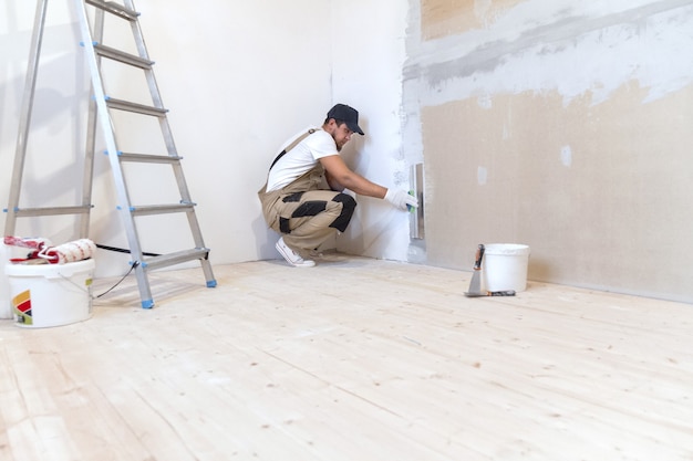 Pintor com uma espátula nas mãos faz reparos em casa. Conceito de renovação de sala.