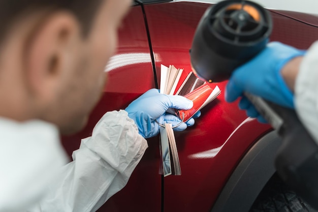 Pintor de automóveis com lâmpada colorista e amostras que selecionam o tom da pintura do carro