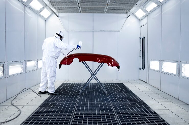 Foto pintor de automóveis com roupa de proteção e pintura de máscara de pára-choque automotivo com pintura metálica e verniz em oficina de câmara.