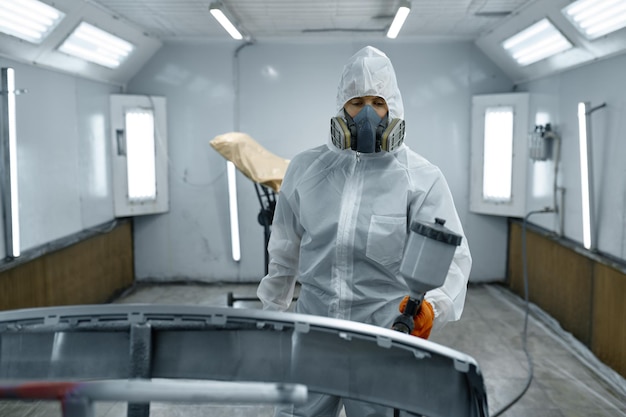 Pintor de carro vestindo roupas de proteção, máscara de pintura de peça de automóvel usando pulverizador