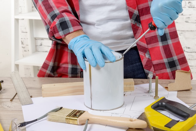 Pintor de casa abre uma lata de tinta com uma chave de fenda