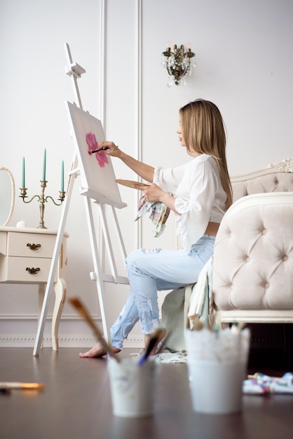 Pintor de dibujo en el estudio de arte con caballete. Retrato de una mujer joven pintando con pinturas al óleo sobre lienzo blanco, retrato de vista lateral