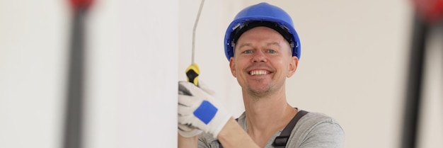 Pintor feliz em chapéu duro pinta a parede com tinta branca e olha para o estande do decorador da câmera