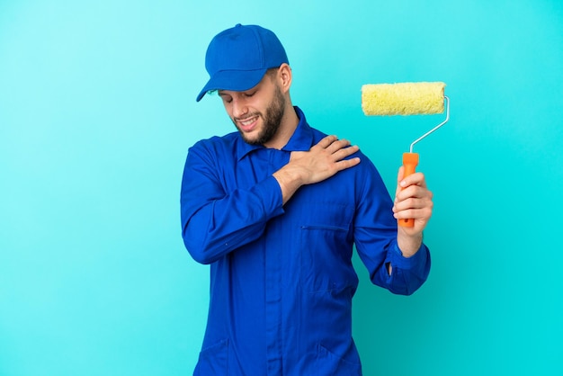 Pintor hombre caucásico aislado de fondo azul que sufre de dolor en el hombro por haber hecho un esfuerzo