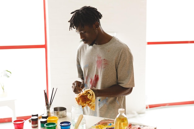 Pintor masculino afro-americano no trabalho limpando as mãos no estúdio de arte. criação e inspiração em ateliê de pintura de artistas.