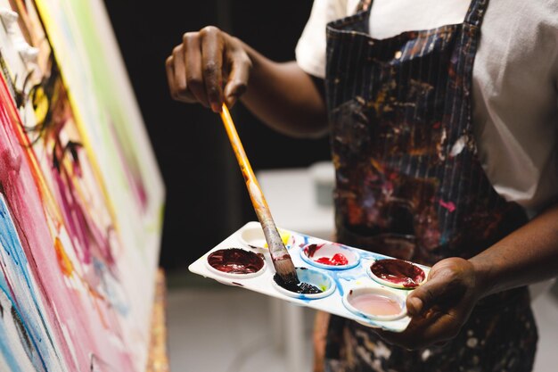 Foto pintor masculino afro-americano trabalhando pintando sobre tela em estúdio de arte. criação e inspiração em ateliê de pintura de artistas.