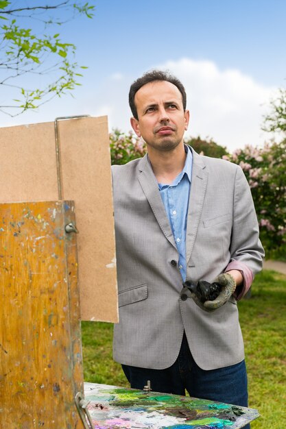 Pintor masculino alegre trabajando en un caballete y pintura de caballete con óleos y acrílicos durante una clase de arte