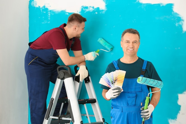 Pintor masculino en uniforme con muestras de paleta de colores y cepillo de rodillo en el interior