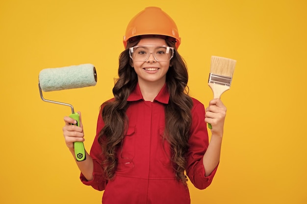 Pintor na oficina Renovação e reparo Menina adolescente no capacete com pincel de pintura Criança no capacete Pintor construtor de criança no canteiro de obras Emoções positivas e sorridentes felizes da menina adolescente