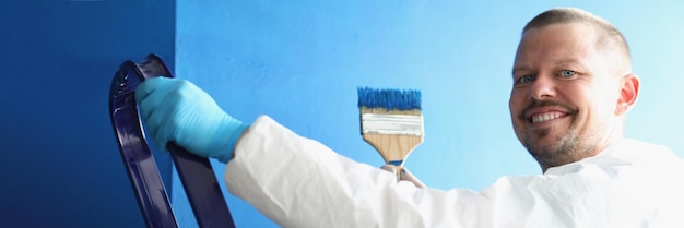 Pintor segurando um pincel coberto de azul para pintar paredes de trabalhador de uniforme