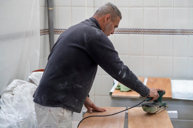 Pintor trabajando en muebles de madera lijándolos para aplicar pintura