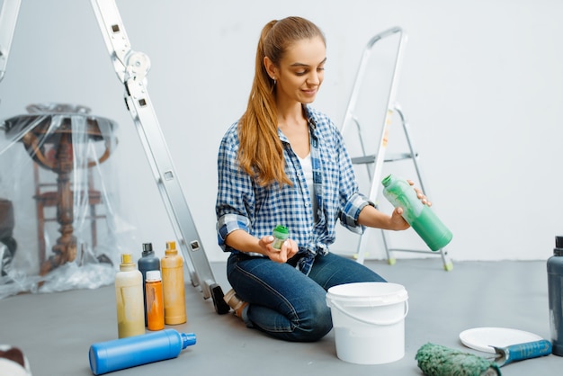 Pintora de casas mezcla pinturas antes de pintar. Reparación de viviendas, mujer feliz haciendo renovación de apartamentos