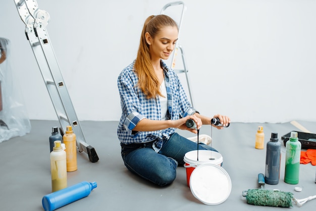 Pintora de casas mezcla pinturas antes de pintar. Reparación de viviendas, mujer feliz haciendo renovación de apartamentos