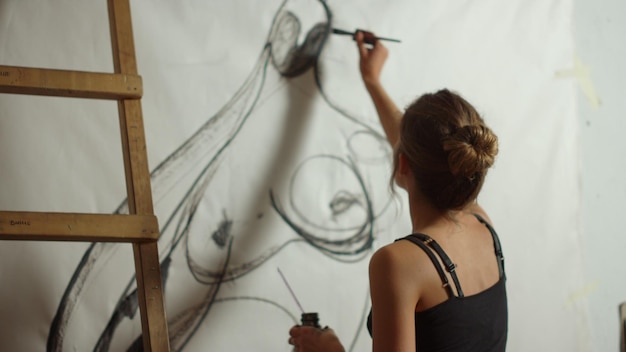 Pintora contemporânea criando obra-prima para exibição em estúdio de arte Vista traseira de uma garota inspirada desenhando em tela dentro de casa Artista feminina talentosa usando tinta preta para pintar na oficina